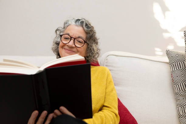 istock Smiling mature woman sitting on a sofa and reading a book 2018019444