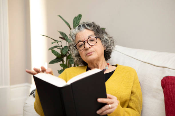 istock Mature woman sitting on a sofa and reading a book 2018020287