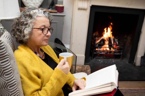 istock Mature woman sitting on a sofa with a coffee and reading a book 2018021351