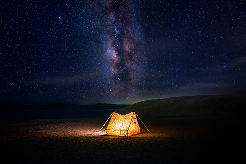 Camping under stars, night sky in the desert, the Milky Way, tents glowing from the inside. Vacation holidays in nature. Sleep under sky. High quality photo