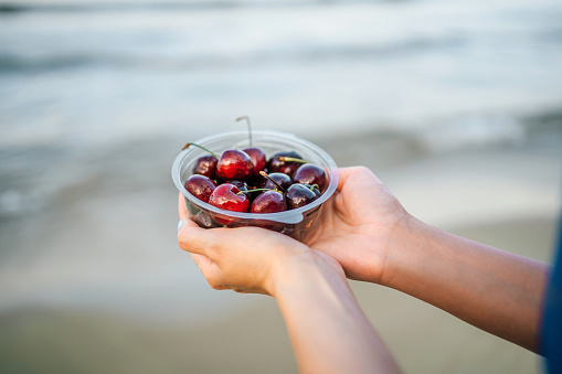 Bowl of juicy cherries in the female hands at the beach