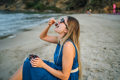 Young beautiful woman eating cherries on the beach
