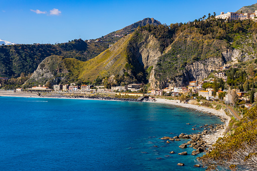 Taormina, Sicily, Italy - February 15, 2023: Panoramic view of Taormina shore at Ionian sea with Castello Saraceno castle, Giardini Naxos and Villagonia towns in Messina region