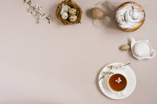 istock Easter cake, eggs, a cup of tea, sweets, branches of a flowering apple tree and feathers on a beige background. Copy space, flat lay 2018067989