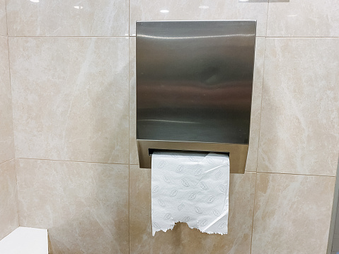 A rectangular wooden fixture holds a roll of toilet paper in a bathroom with hardwood flooring. The dispenser contrasts against the transparency of glass and the use of concrete as a building material.