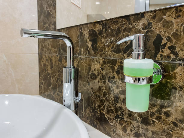 A plumbing fixture comprising a bathroom sink attached to the wall, with a soap dispenser for dispensing fluid located nearby.