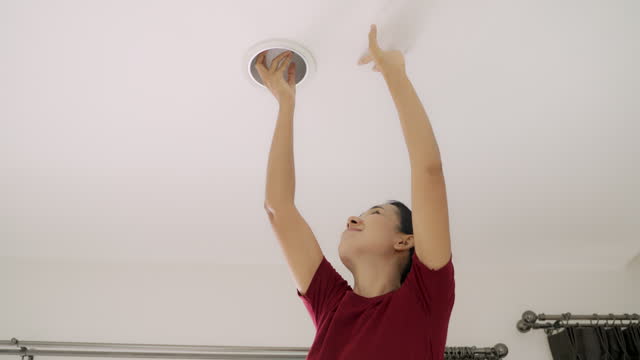 Asian woman changing LED light bulb at home with herself.