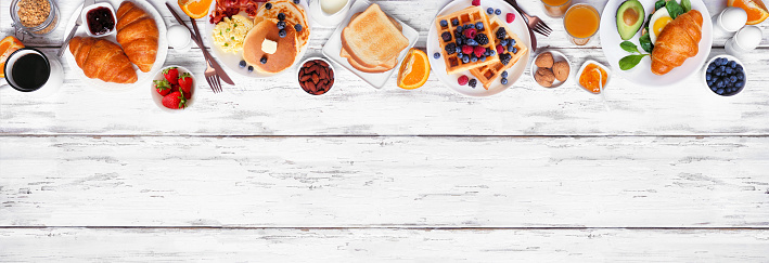 Breakfast or brunch top border on a white wood banner background. Above view. Selection of sweet and savory food items.
