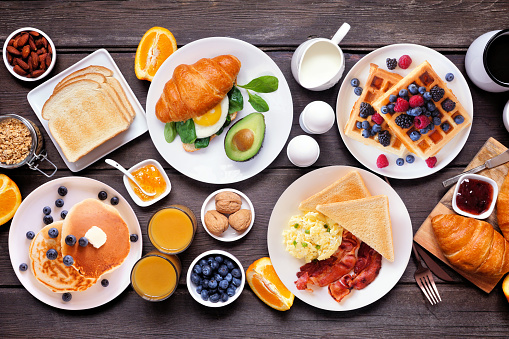 Breakfast or brunch table scene on a dark wood background. Above view. Assortment of sweet and savory food items.