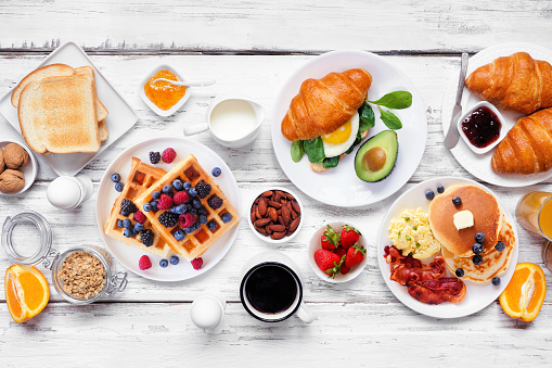 Breakfast or brunch table scene on a white wood background. Top down view. Assorted sweet and savory food items.