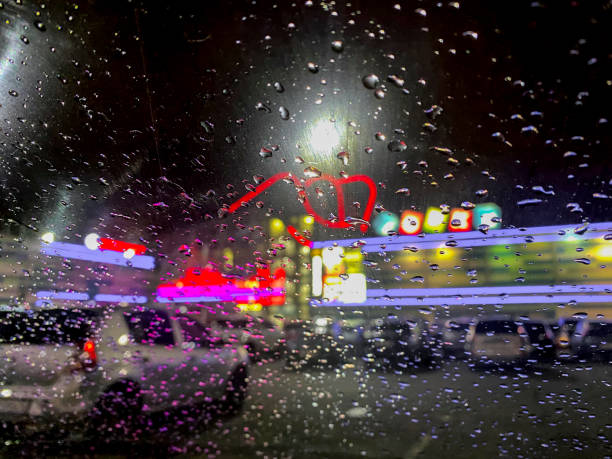 Rain drops on the glass. Blurred background of traffic jam at night