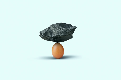Stone balances on an egg on a blue background. Insurance, concept. Balance and strength, creative idea. Strong creative egg