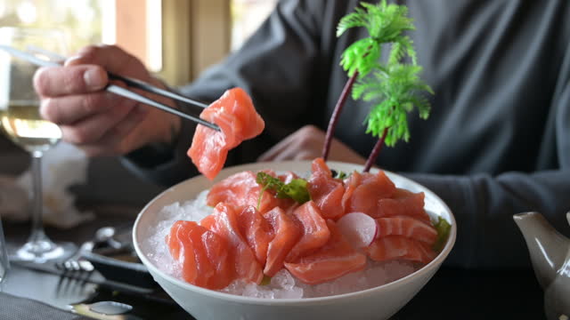 unrecognizable man eating salmon sashimi in a restaurant.