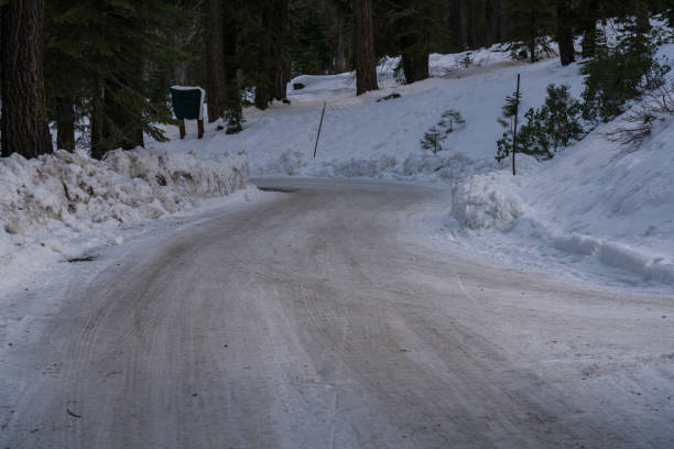 Icy snow covered road leading to parking area through forest.