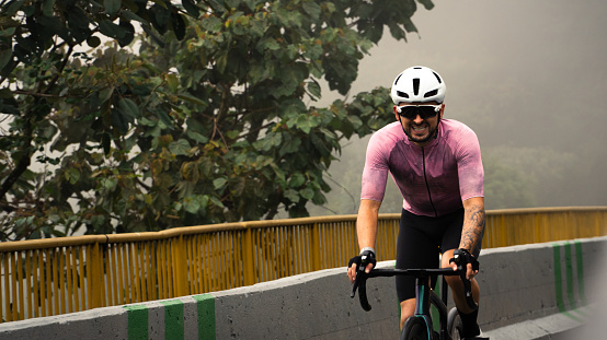professional cyclist training cycling with a face of pain and tiredness in the middle of the fog on a climb in Colombia
