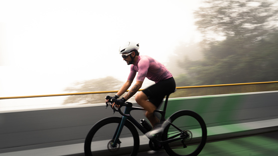 male cyclist with white helmet and pink jersey in side view riding bike on a famous street in colombia on a cold and foggy day. Dynamic and moving picture