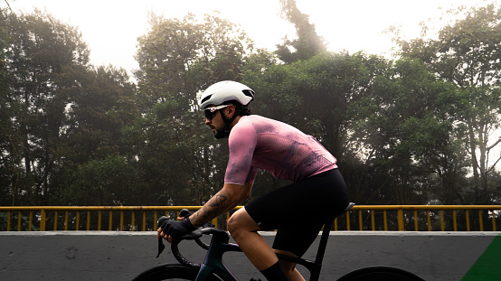 male cyclist with white helmet and pink jersey in side view riding a bicycle on a famous street in colombia on a cold and foggy day.