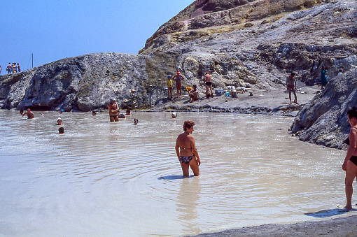 Vulcano Island, Aeolian Islands, Sicily, Italy - August 10, 1980: tourists and bathers immerse themselves in a pool of warm thermal mud on the island of Vulcano, Aeolian Islands, Sicily, Italy