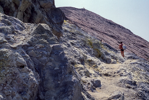 Vulcano Island, Aeolian Islands, Sicily, Italy - August 10, 1980: a hiker climbs to the top of the volcano crossing the ancient lava flows during the ascent to the volcano crater on the island of Vulcano, Aeolian Islands, Sicily, Italy