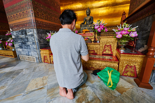 Bangkok, Thailand - August 26, 2023: a kneeling man pray in front of a Buddha statue at Wat Pho temple.