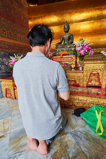 Bangkok, Thailand - August 26, 2023: a kneeling man pray in front of a Buddha statue at Wat Pho temple.