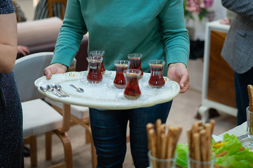 Woman holding tray containing glasses of Turkish tea at a house party