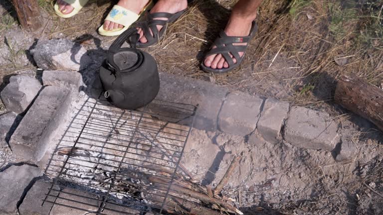 Couple in Love Drinks Hot Coffee in a Mug near a Smoking Campfire in the Forest