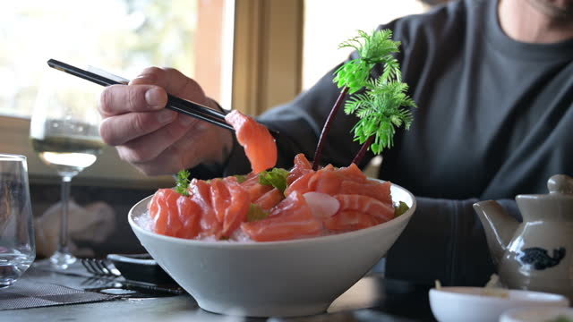 Man eating salmon sashimi in a restaurant.