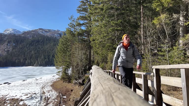 A man with a backpack walks along a wooden bridge, sunny day, forest and mountains