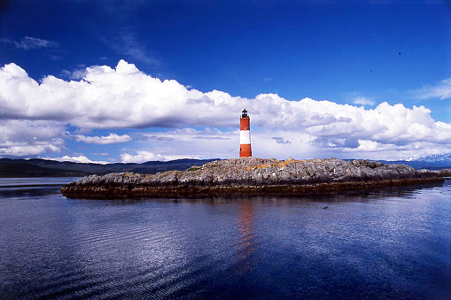 A small island in the Beagle Channel near Ushuaia, Argentina, with a popular tourist attraction of Les Eclaireurs (The Scouts) Lighthouse. A cruise ship and rainbow are in the background.