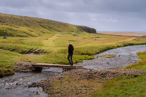 Adult man crossing a stream  on a bridge near Rauðasandur beach in the Westfjords, Iceland