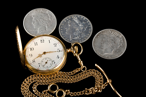 old pocket watch with train engraving on the cover, patinated brobce color, open with chain arranged in a spiral on beige background close-up view