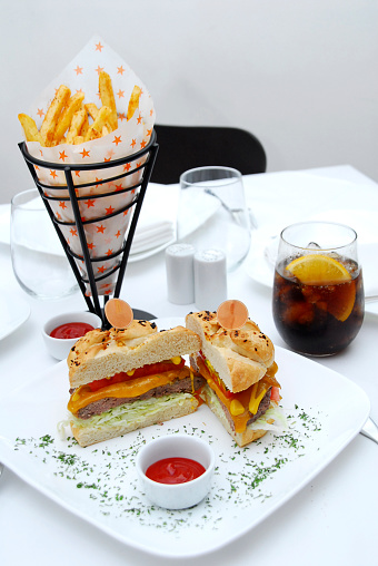 hamburger with fries, cola and toppings on a restaurant table, white background