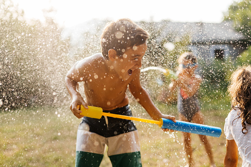 Children having fun with squirt gun, playing water gun fight in the backyard