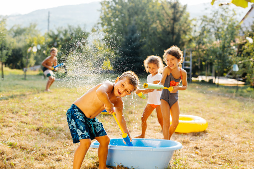 Children having fun filling squirt gun with water and spraying each other on a hot summer day