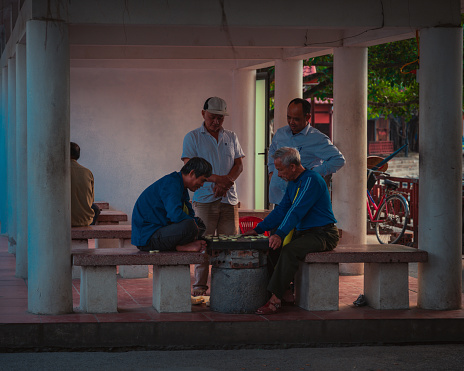 Two man battle in a game of chess in a public space in Tam Coc Vietnam. Two othes watch and criticize their moves.