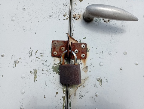 A padlock hangs on the rusty metal hinges of the door. The metal door is locked.