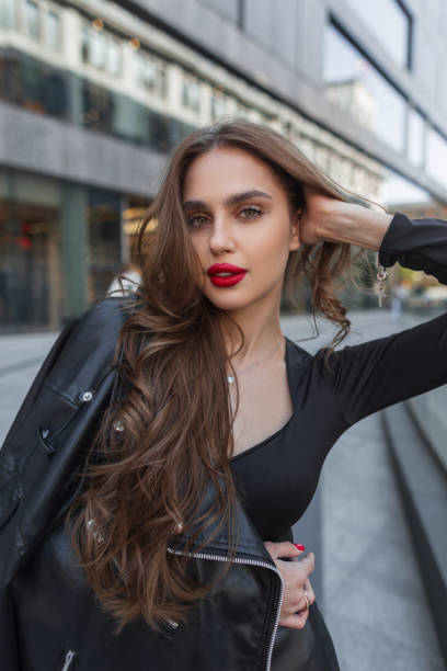 istock Fashionable young glamour pretty chic lady with red lips in black stylish clothes with leather jacket walks in the city 2018484850