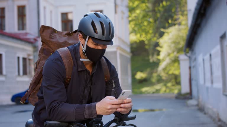 Delivery man courier with face mask and bicycle using smartphone in town.