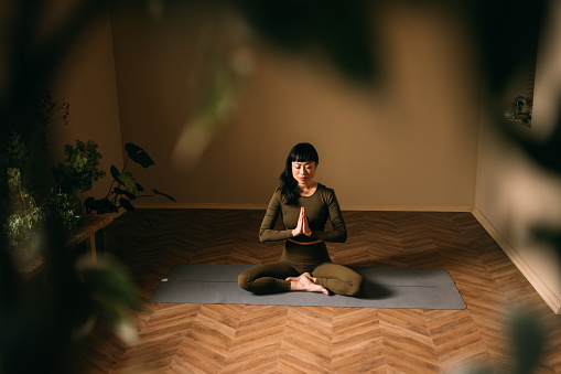 Woman meditating in lotus pose with eyes closed, exuding calm and focus in a yoga studio.