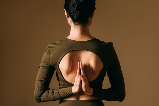 Rear view of a woman in a yoga Namaste pose, symbolizing peace and spirituality.