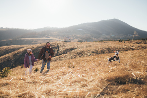 Cheerful family walking with their happy dog on a golden field, embracing nature and togetherness.