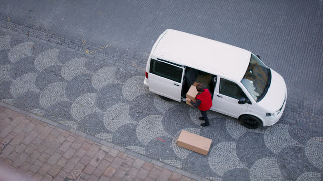 Aerial view of delivery man courier with car in town, taking out parcel boxes.