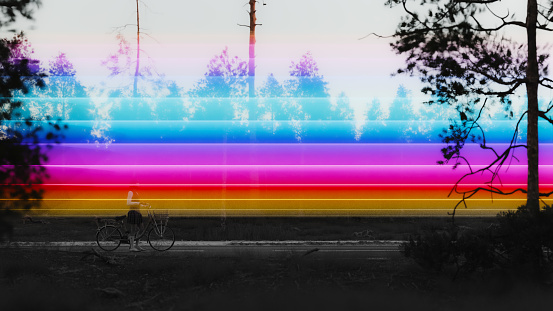 A multi colored light trail passing over a person cycling on a rural road. All objects in the scene are 3D