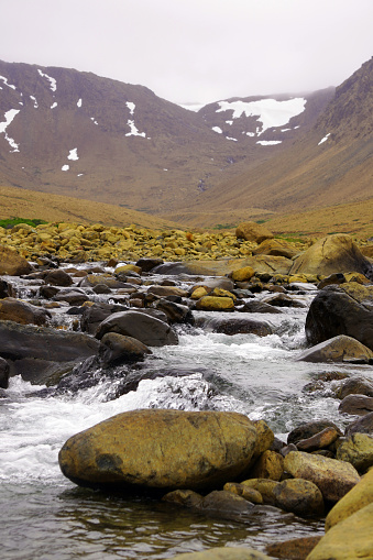 Stream tumbling over rocks in the foreground with desolate mountain slopes in the background in the Tablelands region of Gros Morne National Park on Newfoundland's western coast