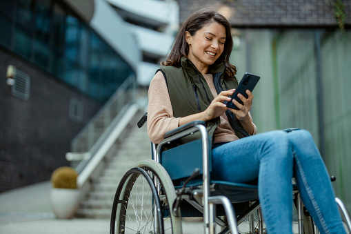 Happy Handicapped Woman in Wheelchair Using Smartphone on City Street