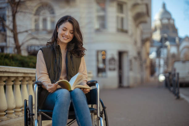 mujer discapacitada alegre en silla de ruedas con libro al aire libre - outdoors book reading accessibility fotografías e imágenes de stock