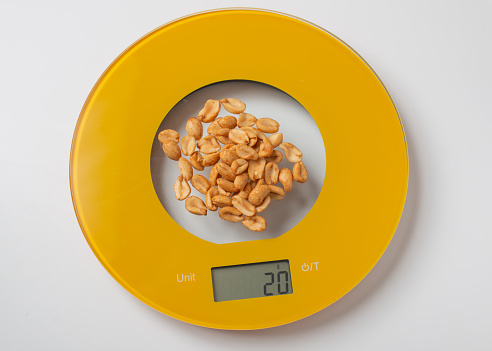 A handful of peanuts weighted on yellow round kitchen electronic scale