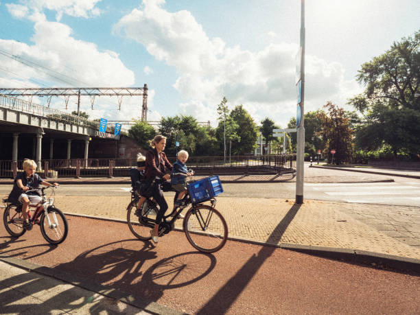 Haarlem, Netherlands - Aug 17, 2019: Young single mother carrying two kids young boys on her bicycle on the dedicated lane with another child riding a bike next to her