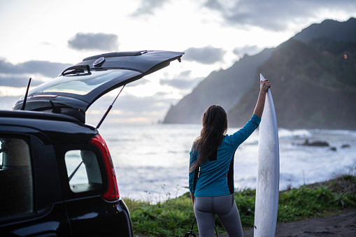 Middle aged woman near her car goes surfing at sunset. Getting away from it all.